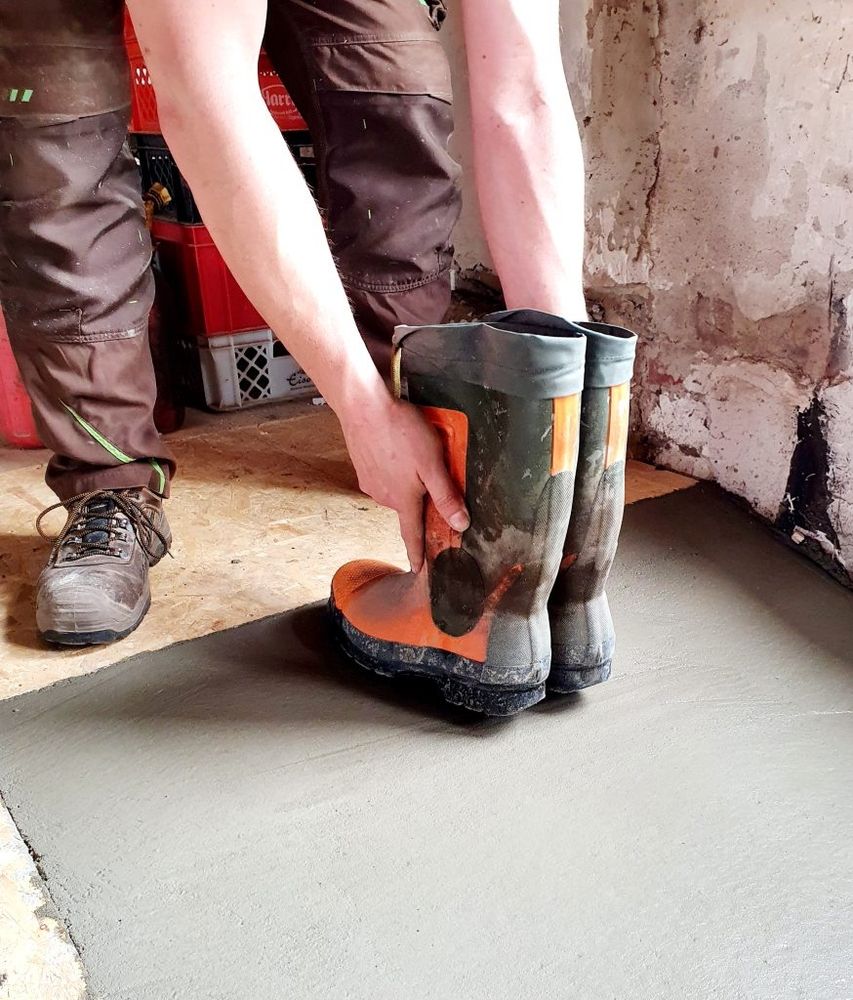 Arbeiter zieht Gummistiefel an, während er frischen Beton verlegt.