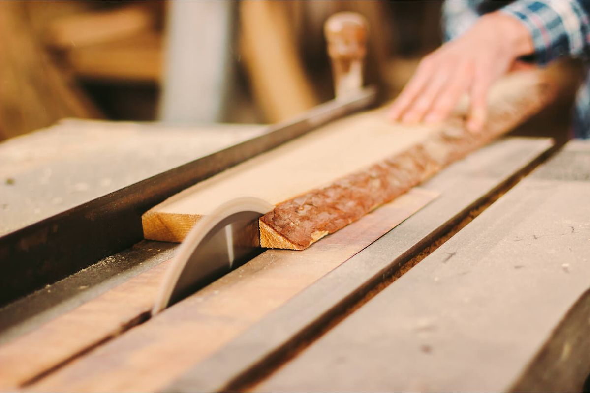Hand, die ein Stück Holz auf einer Tischsäge führt.