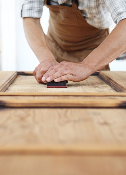 Handwerker schleift Holzoberfläche mit Schleifpapier.
